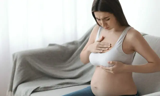 Ciężarna kobieta z bólem dotyka piersi, czując pierwsze oznaki siary.