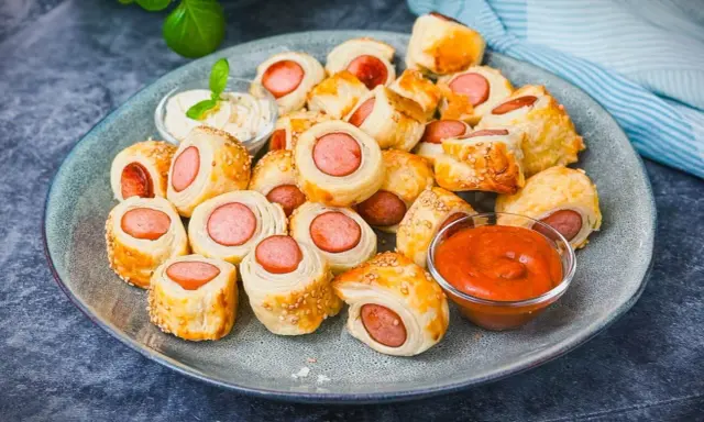 Leckeres Fingerfood für den Sommer: Würstchen im Blätterteig mit Sesam, serviert mit Dip und Ketchup.