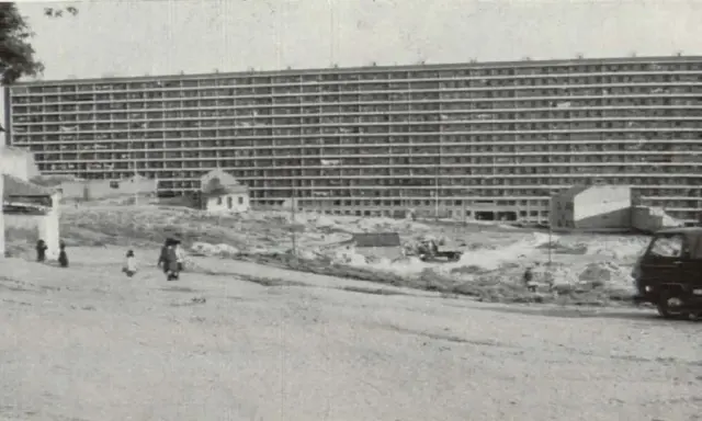 Edificio masivo de apartamentos en construcción, con obreros y vehículos en el sitio. Imagina cómo se veía cuando se inventó el cemento.
