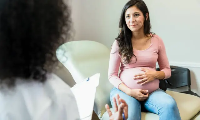 Schwangere Frau im Gespräch mit Arzt. Sie fragt sich, wie lange dauert eine einleitung, während sie ihren Bauch streichelt.
