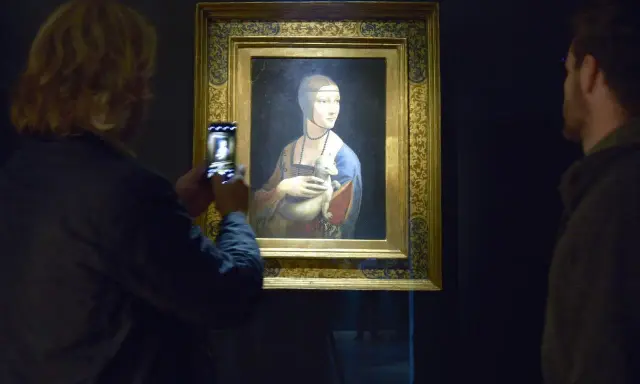 Dama z gronostajem Leonarda da Vinci, uwieczniona na zdjęciu przez turystkę. Obok obrazu stoi mężczyzna.