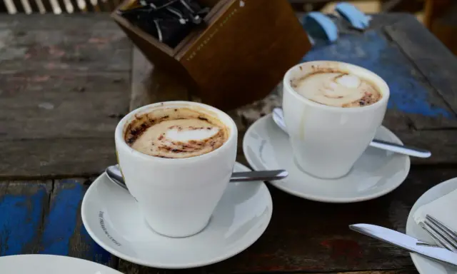 Zwei Tassen Kaffee Latte mit Milchschaum und Kakao-Muster auf einem Holztisch.