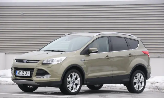 Złoty Ford Kuga 2.0 TDCI z polskimi tablicami WE 258FF zaparkowany na tle industrialnej ściany.