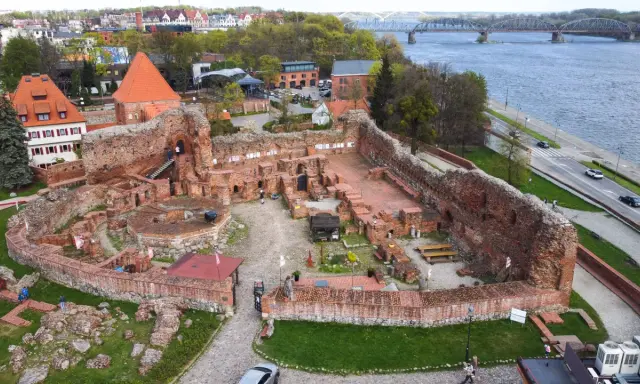 Ruiny zamku bierzgłowskiego z czerwonej cegły, z widokiem na rzekę i most.