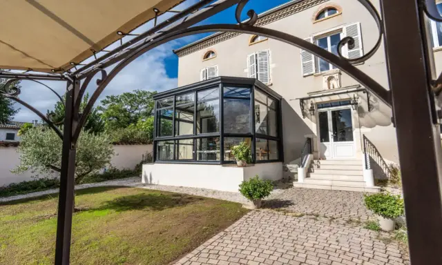 Une élégante véranda moderne s'intègre à une maison de campagne. La surface de plancher pavée mène à des marches menant à la porte d'entrée.