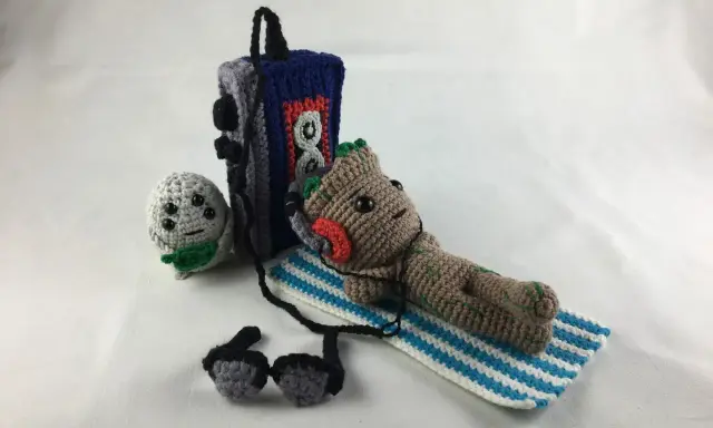 Amigurumi Baby Groot tumbado con auriculares junto a un reproductor de música y un pequeño personaje gris.