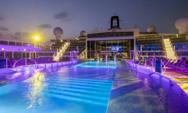 Piscine illuminate con luci viola e blu sulla MSC World Europa, con sdraio e scale illuminate.