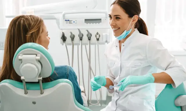 Uśmiechnięta dentystka w rękawiczkach rozmawia z pacjentką. Może właśnie omawia antybiotyk na zęba.