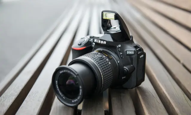 Czarny aparat Nikon D5600 z wysuniętą lampą błyskową leży na drewnianej ławce. Idealny do nikon d5600 test.