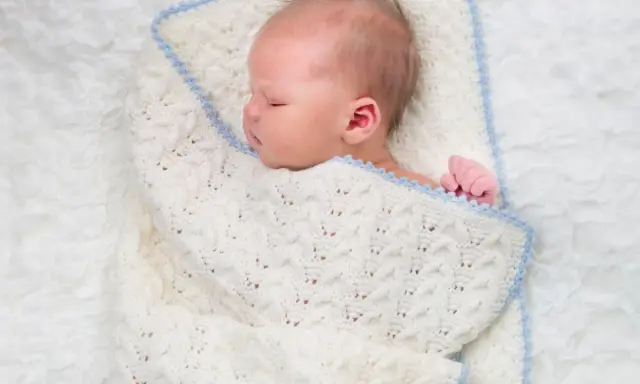 Sover sött i en stickad filt. Att knyta sjal bebis är ett mysigt sätt att hålla dem varma.