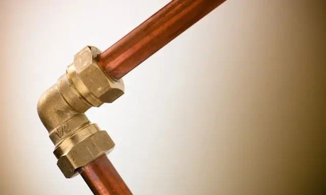 Un raccord coudé en laiton relie deux tuyaux en cuivre, illustrant une plomberie sans soudure efficace et durable.