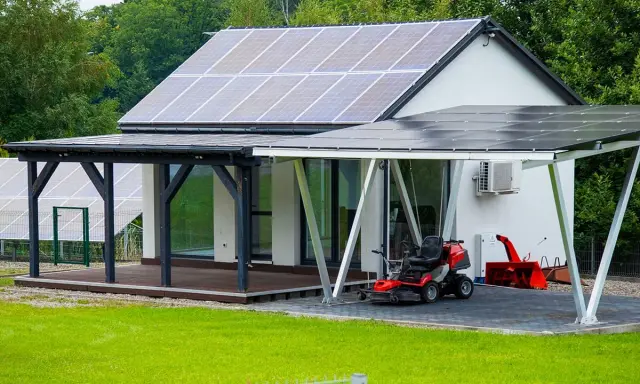Maison moderne avec implantation panneau solaire sur le toit et le carport. Une tondeuse et un souffleuse à neige sont garés sous le carport.