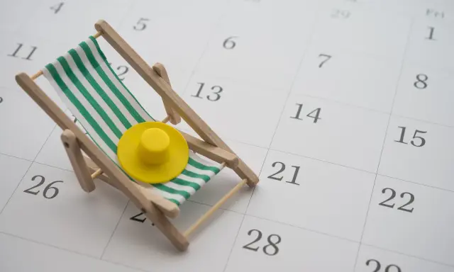 Miniaturowa leżanka plażowa z zielono-białymi pasami i żółtym kapeluszem na tle kalendarza.