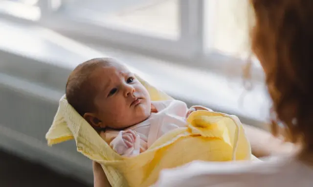 Malutki noworodek pierdzi, ale nie robi kupy. Otulony w żółty kocyk, patrzy z uwagą.
