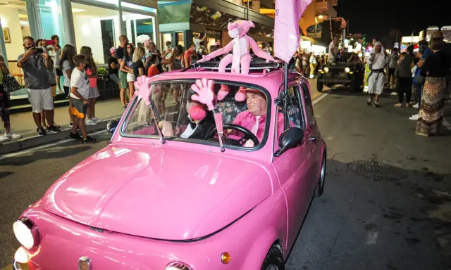 Un'auto rosa shocking sfila a Rimini durante la Notte Rosa, con un pupazzo a forma di pantera rosa sul tetto e un uomo al volante vestito a tema.