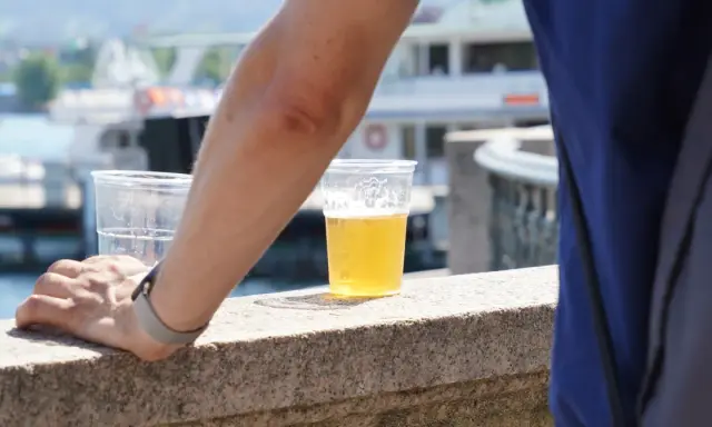 Ręka opiera się o kamienny murek, obok piwo w plastiku. Może to początek drogi do spadku wagi po odstawieniu piwa.