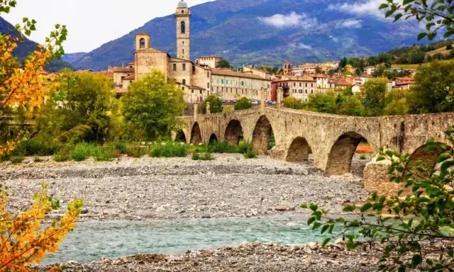 Ponte Gobbo a Bobbio, borgo dei borghi, con il fiume e le montagne sullo sfondo.