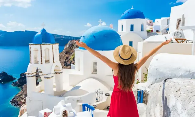 Kobieta w czerwonej sukience i kapeluszu cieszy się widokiem na Santorini. Idealne miejsce, gdzie do Grecji na wakacje!
