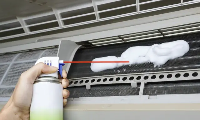 Mano rociando espuma para limpiar aire acondicionado unidad interior.