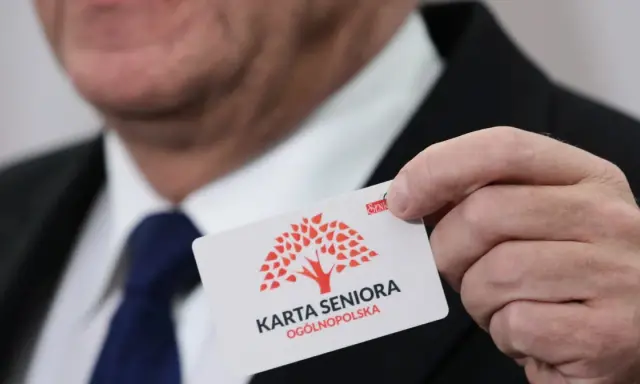 Dłoń trzyma białą kartę z czerwonym drzewem i napisem "KARTA SENIORA OGÓLNOPOLSKA".