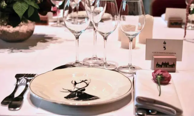 Un élégant dressage à la française pour un dîner de gala, avec une assiette ornée d'un cerf, des verres à pied et une carte de visite pour le Grand-Duc de Luxembourg.