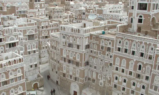 Ein malerisches arabisches Haus mit kunstvollen weißen Verzierungen und vielen Fenstern, eingebettet in eine Stadt mit ähnlicher Architektur.