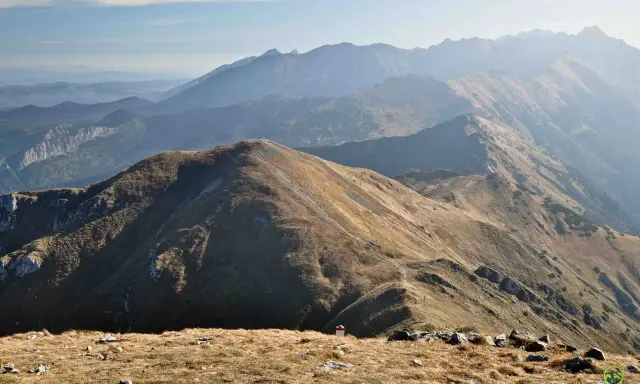 Widok na pasmo górskie Tatr. W oddali widać kolejne grzbiety górskie, a na pierwszym planie ścieżki i kamienie. Trasy Tatry zachęcają do wędrówki.