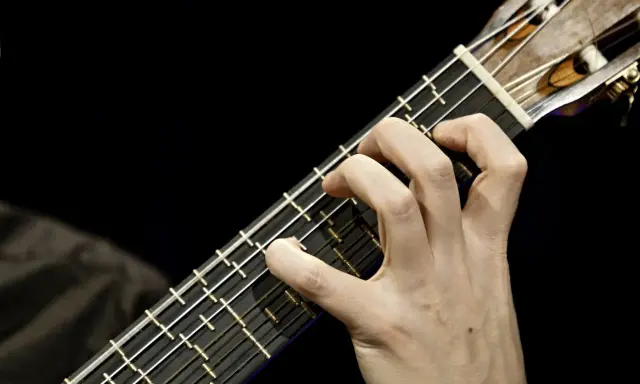 Main d'un guitariste jouant sur une microtonal guitar, ses doigts effleurant les cordes sur un manche sombre.