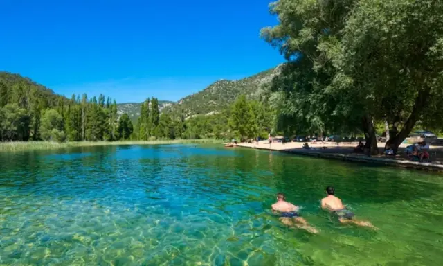 Dos hombres nadan en la cristalina piscina natural Cañamares, rodeada de vegetación y montañas.