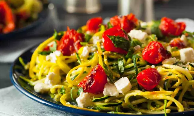 Pasta con verdure: spaghetti di zucchine, pomodorini confit, feta e basilico fresco su un piatto blu.