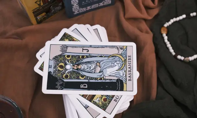 Karty tarota ułożone na brązowym materiale. Jedna karta, przedstawiająca postać z księżycem i owocami, jest na wierzchu. To idealny obrazek na **tarot na tydzień**.