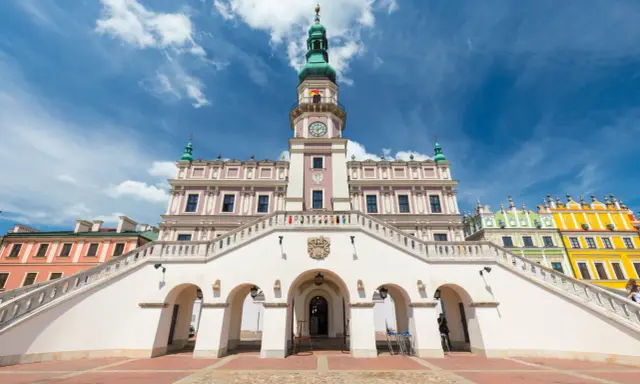 Zamość rynek: Ratusz z imponującymi schodami i kolorowe kamienice pod błękitnym niebem.