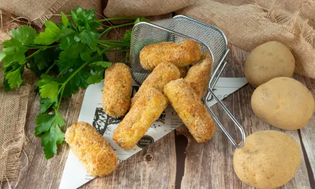 Crocchette di patate in friggitrice ad aria, dorate e croccanti, pronte per essere gustate. Accanto, patate fresche e prezzemolo.