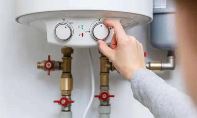 Main d'une personne ajustant le thermostat d'un chauffe-eau, contrôlant la pression de l'eau et la température.