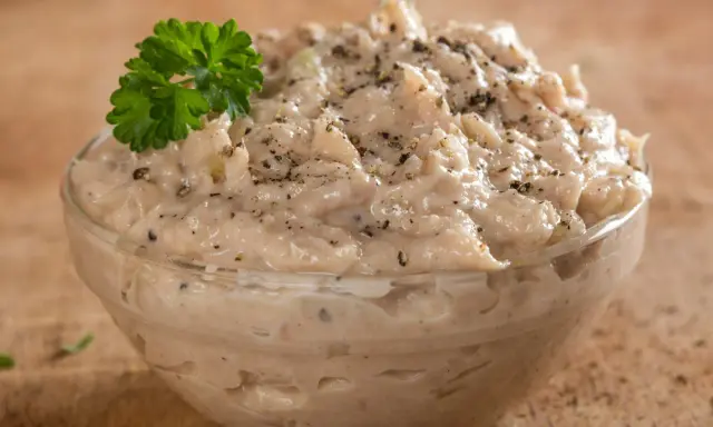 Pyszna pasta z tuńczyka w szklanej miseczce, doprawiona pieprzem i udekorowana gałązką natki pietruszki. Idealna na kanapki.