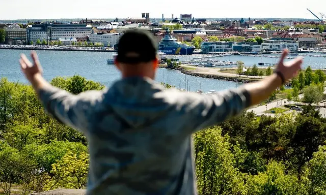 En person med armarna utsträckta njuter av utsikten över en hamn och stad, kanske den soligaste staden i Sverige.