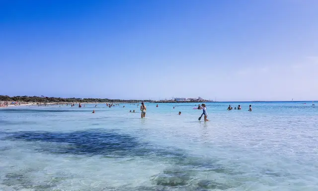 Słoneczny dzień na plaży Es Trenc. Ludzie kąpią się w krystalicznie czystej wodzie, ciesząc się wakacjami.