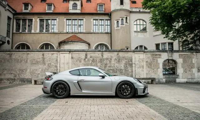 Silberner Porsche GT4 vor historischer Kulisse. Die technischen Daten dieses Sportwagens sind beeindruckend.