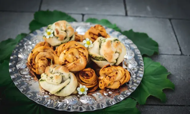 En silverbricka fylld med vackert formade vegetariska pizzabullar, dekorerade med små vita blommor och gröna blad.