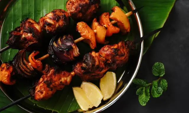 Brochettes de poulet grillées, marinées et savoureuses, avec oignons et poivrons, servies sur une feuille de bananier avec des quartiers de citron.