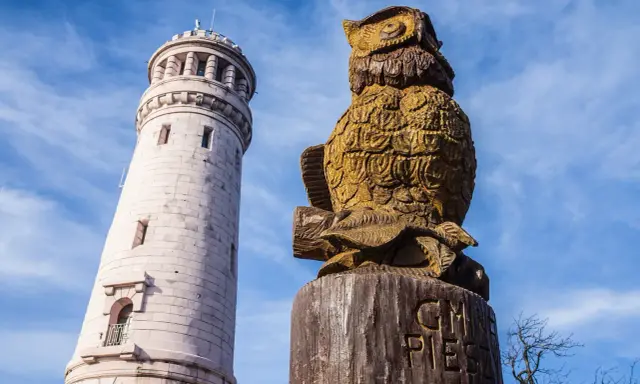 Gdzie są góry? Sowa z drewna i wieża obserwacyjna na tle błękitnego nieba.