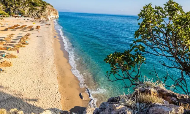 Piękna plaża w Albanii z turkusową wodą i rzędami parasoli. Ceny wakacji w Albanii są przystępne, a widoki zachwycające.