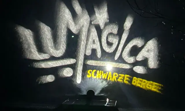 LUMAGICA Schwarze Berge Schriftzug auf Wasserprojektion bei Nacht.
