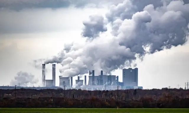 Rauchschwaden steigen aus einem Kraftwerk auf und symbolisieren die historischen CO2-Emissionen, die die Umwelt belasten.