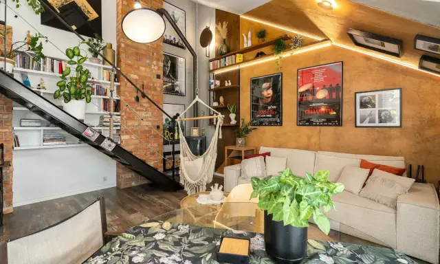 Przytulny mały pokój w stylu loft z ceglaną ścianą, metalowymi schodami, wiszącym fotelem i wygodną kanapą.