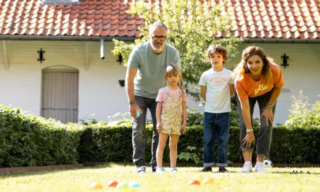Une famille s'amuse dans le jardin avec un jeu de pétanque en ligne. Les boules colorées sont alignées sur l'herbe.