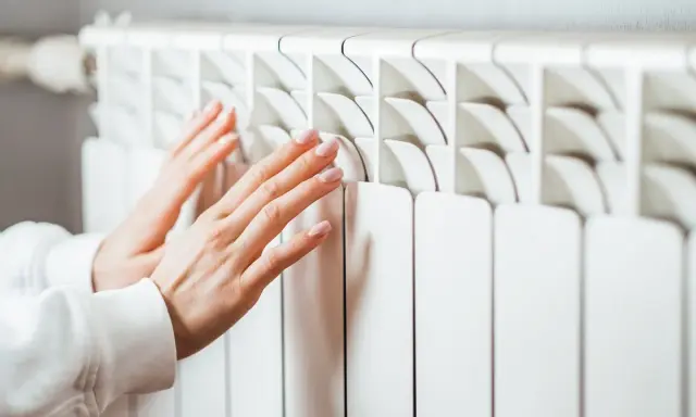 Manos cálidas sobre un convector blanco, sintiendo el calor del invierno.
