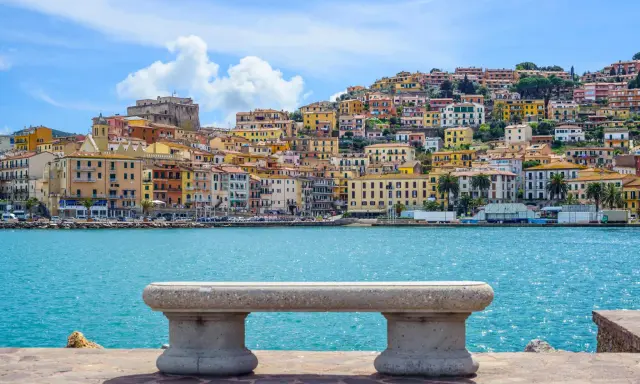Panoramica di Porto Santo Stefano con case colorate a picco sul mare turchese. Un invito a scoprire cosa vedere a Porto Santo Stefano.