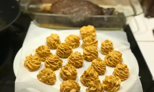 Piped dollops of golden-brown sauce arranged on white parchment paper, with a roasted dish in the background.