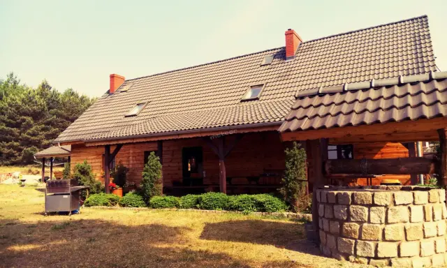 Drewniany dom pod kasztanem, z kamienną studnią i grillem, otoczony zielenią i lasem.